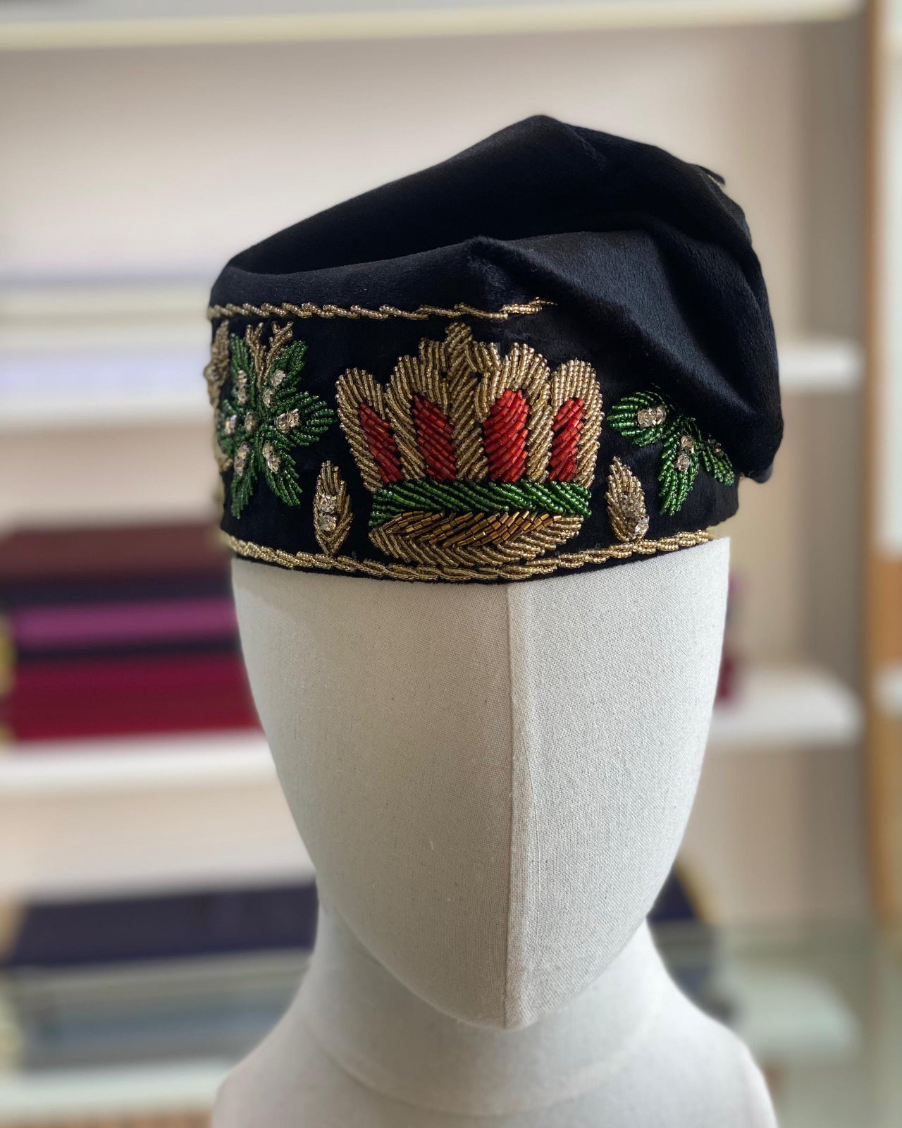 A black cap with intricate beading details displayed on a mannequin head.